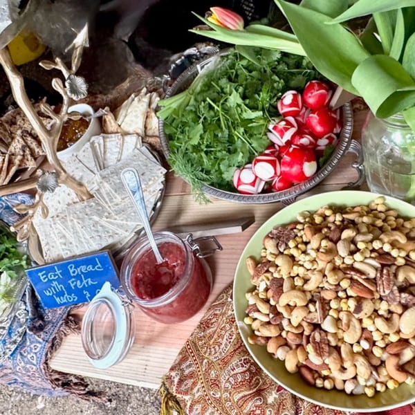 A vibrant spread of flatbread, herbs, radishes, nuts, and jam on a patterned tablecloth.