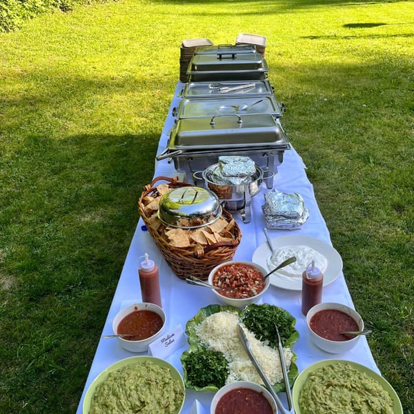 A long outdoor buffet table with Viva Mexicana's Mexican food, including guacamole, salsa, and chips.