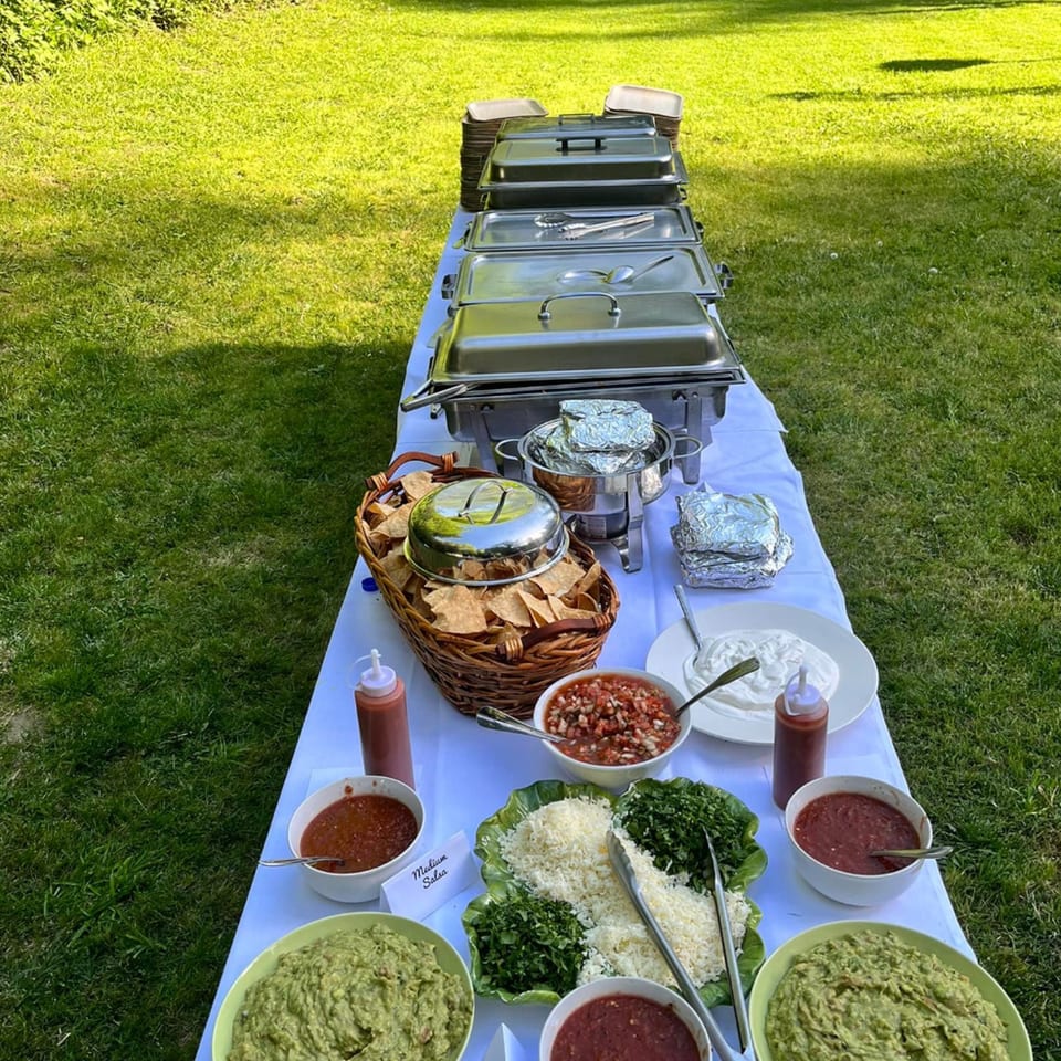 A long outdoor buffet table with Viva Mexicana's Mexican food, including guacamole, salsa, and chips.