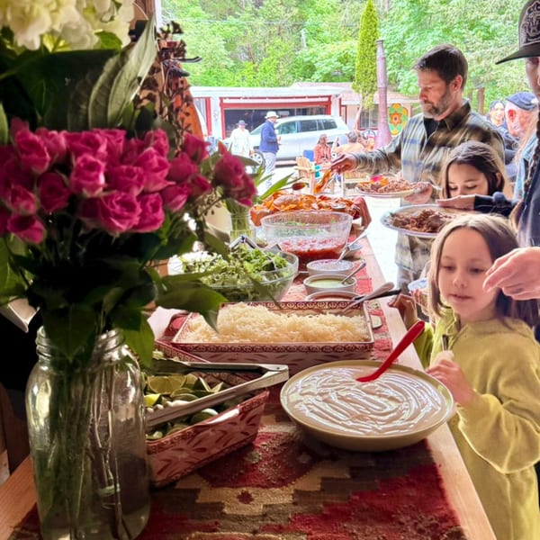 People serving themselves from a buffet table laden with food and flowers at an outdoor gathering.