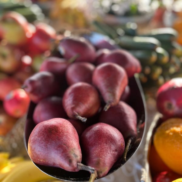 A close-up of a bowl filled with fresh red pears, surrounded by other fruits and vegetables.