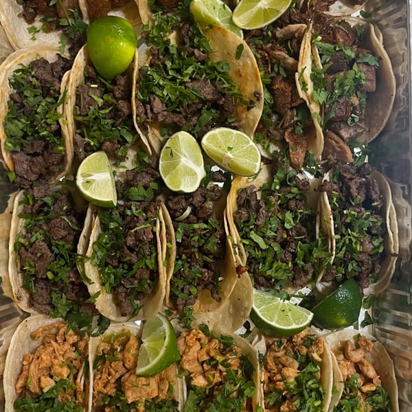 A tray of beef and chicken tacos topped with cilantro and lime wedges.