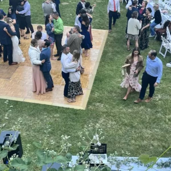 Guests dancing on a wooden dance floor and mingling on a grassy lawn at an outdoor event.